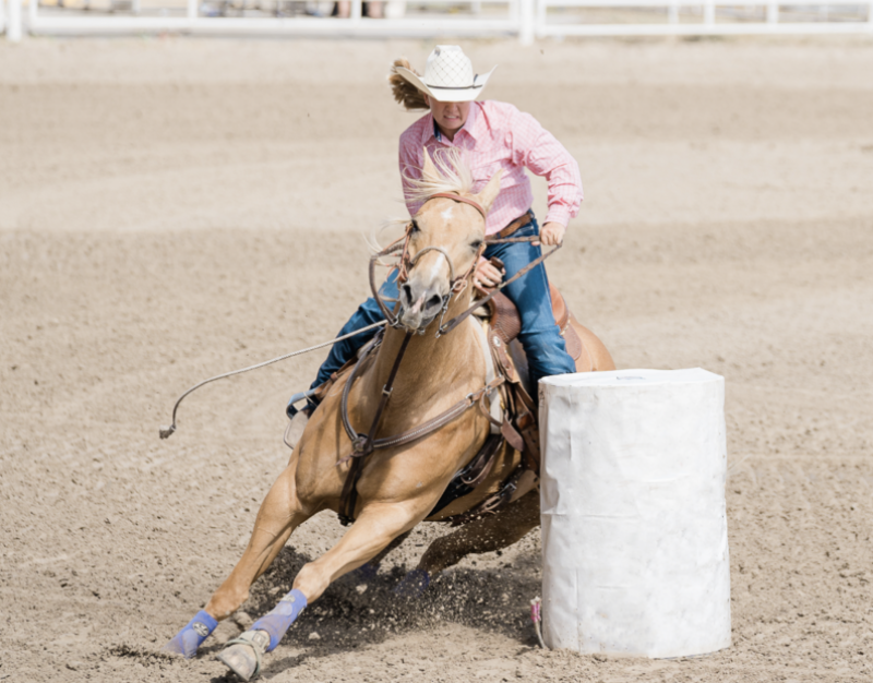 A woman barrel races a palomino horse