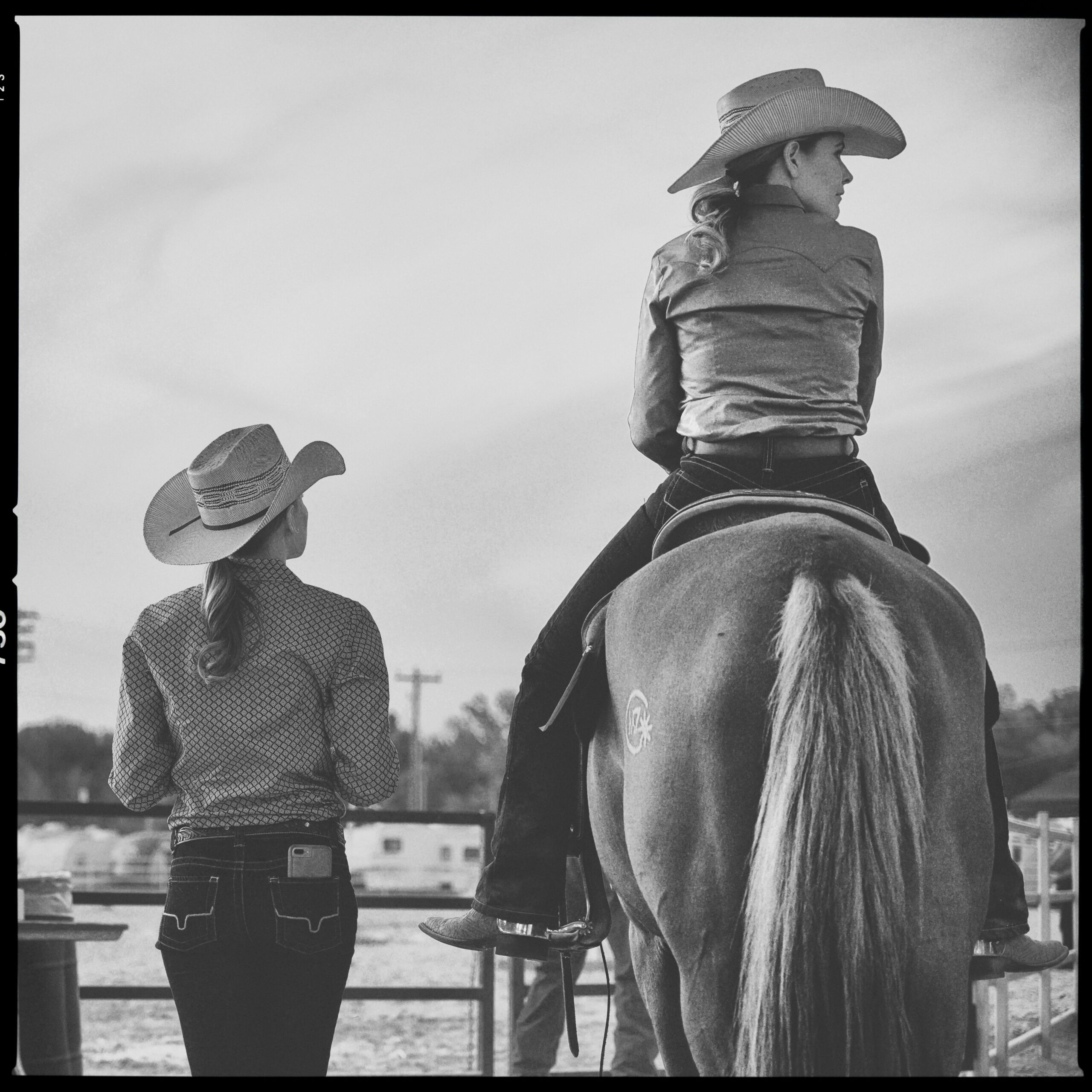 One woman stands at the fence next to a woman on a horse